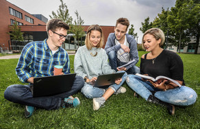 Group learns in the meadow Four students are sitting on the grass and looking in a book.