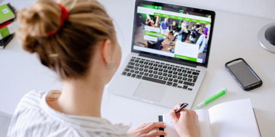 Arbeit am Laptop Am Schreibtisch sitzende Studentin arbeitet am Laptop, daneben liegen Bücher und Stifte.